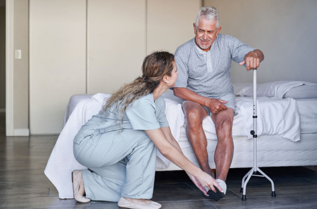 een zorggever helpt de schoenen aandoen van hulpbehoevende oude man